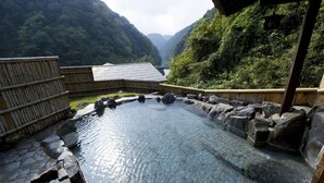 Un onsen japonés tradicional con una piscina de piedra cristalina rodeada de rocas, vallas de bambú y una estructura de madera.