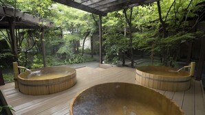 Una terraza de madera con tres jacuzzis rodeados de abundante vegetación.