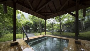 Zona de baño termal de madera con un deck y vistas a un jardín exuberante.