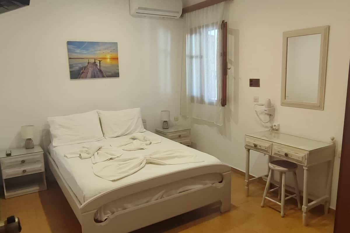A bedroom with a bed, bedside table, desk, chair, and a mirror.