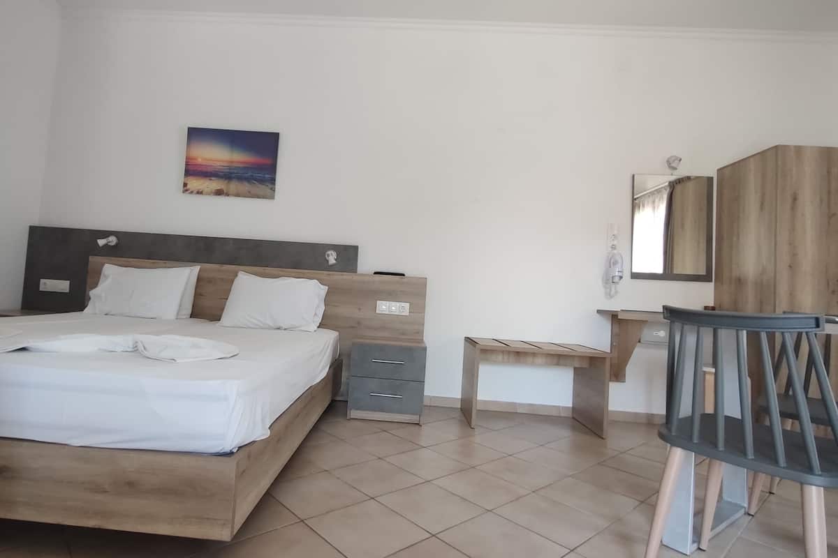 A bedroom with a wooden bed, a small desk, a chair, and a painting on the wall.