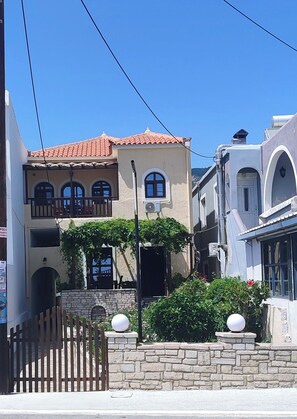 Un edificio a due piani con tetto in tegole, un balcone e un muro in pietra con un cancello.