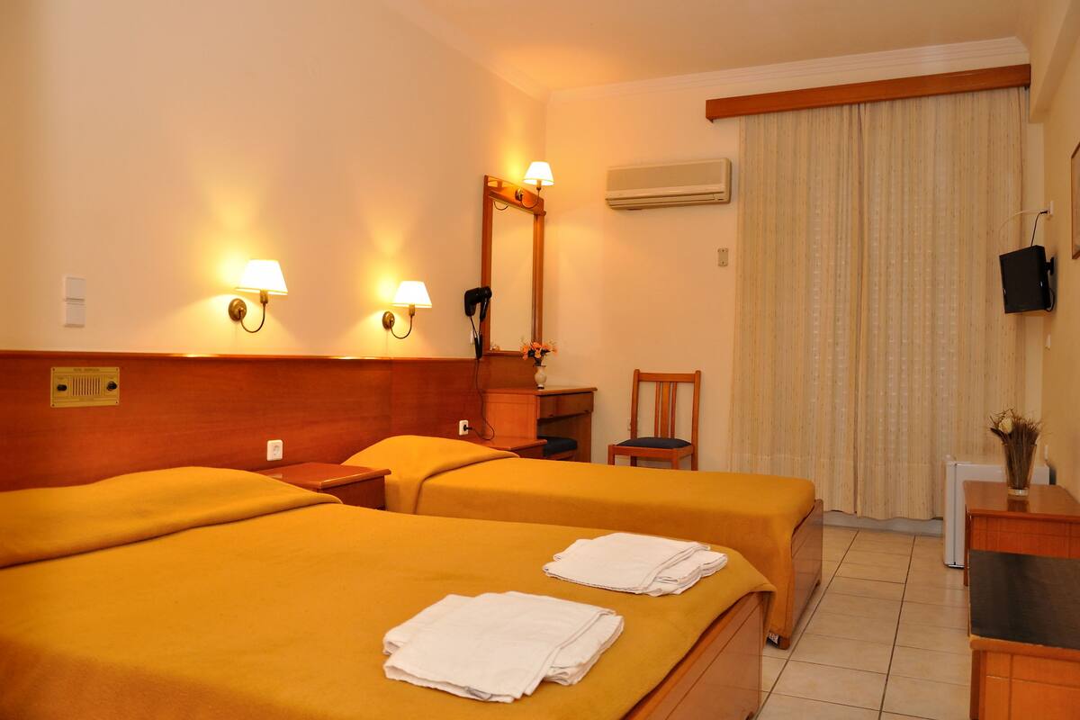 A hotel room with two beds, a desk, a chair, and a TV.