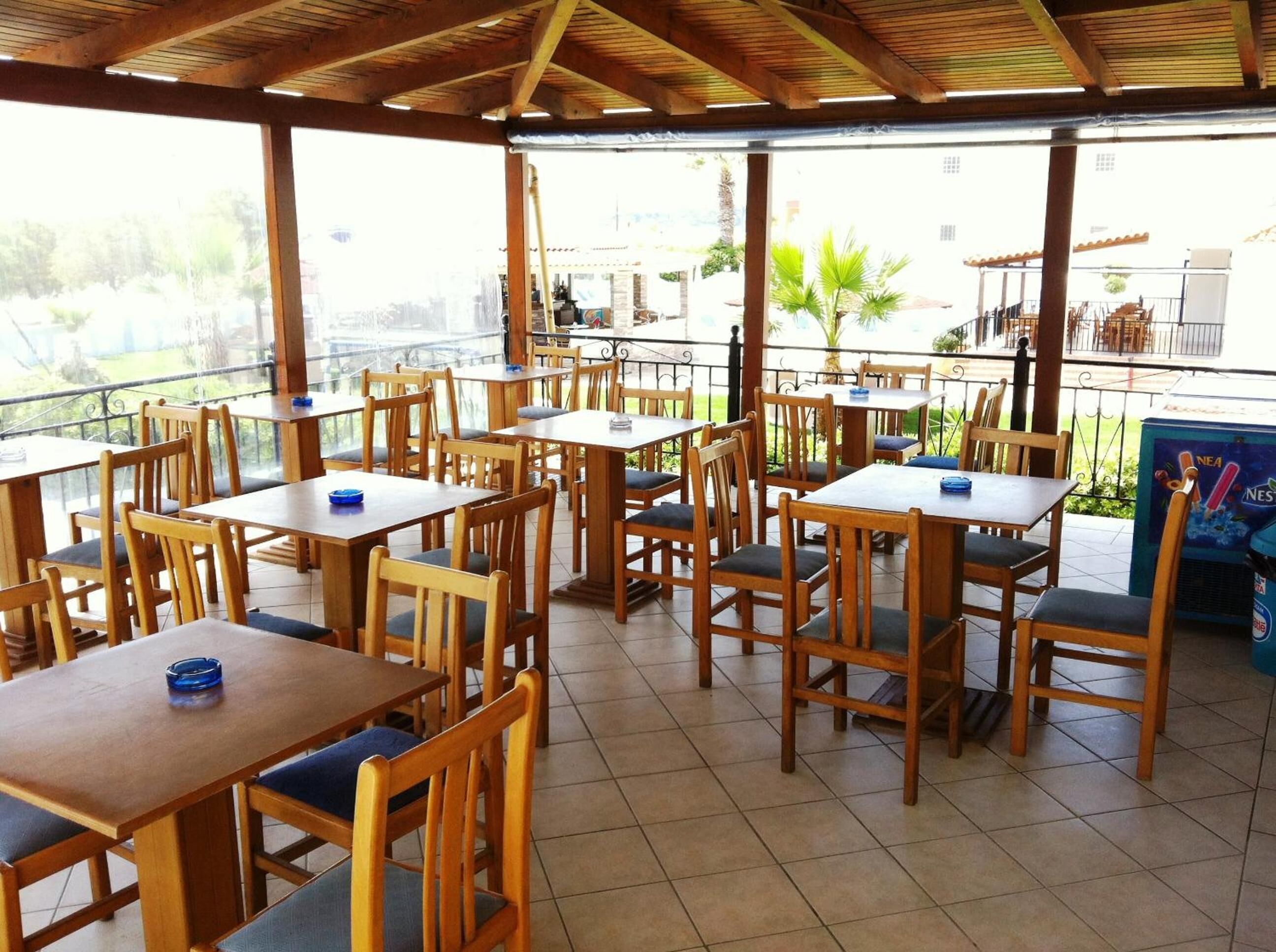 An outdoor cafe with wooden tables and chairs, a tiled floor, and a view of the surrounding area.