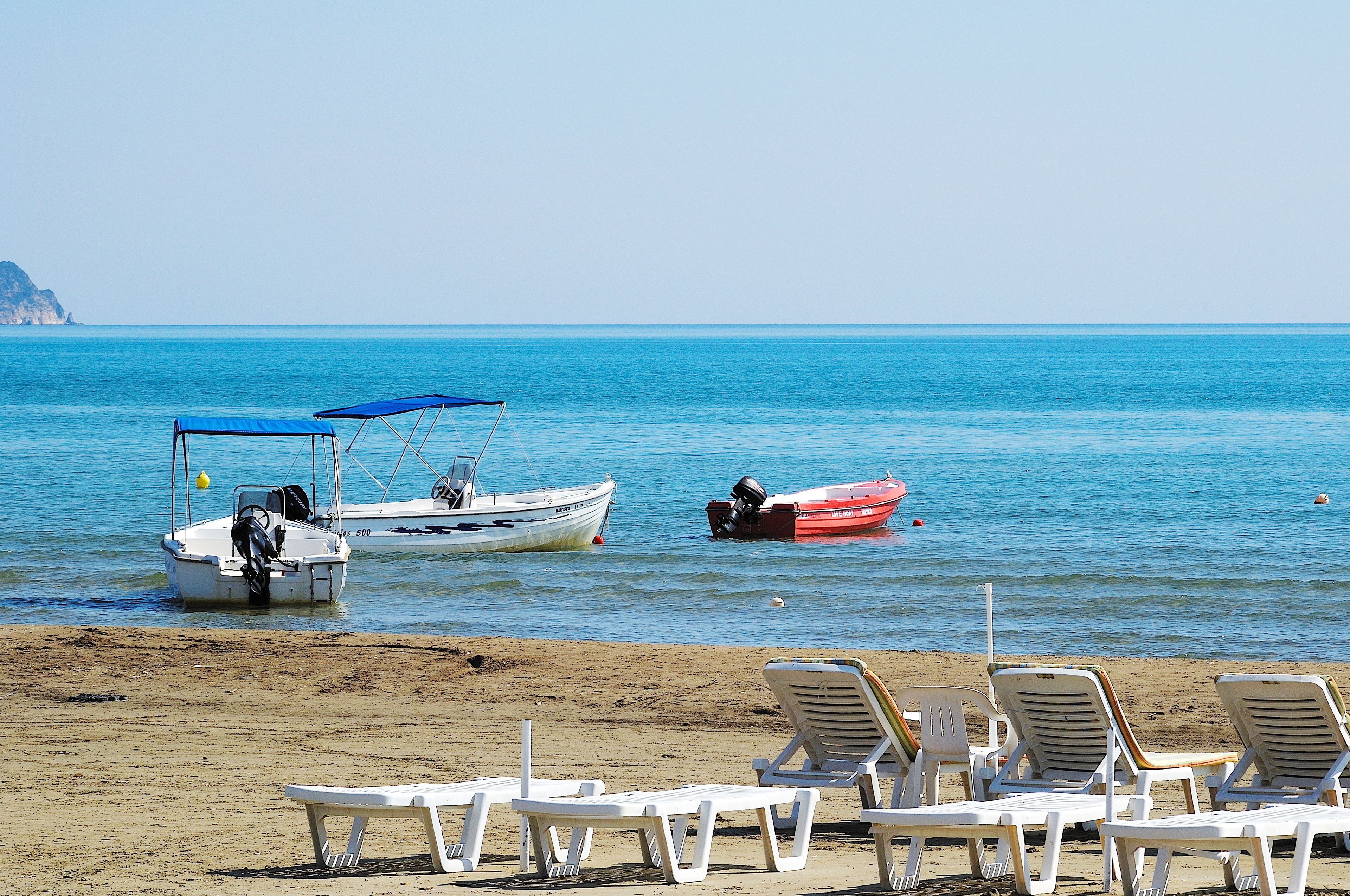 Uma praia com cadeiras de praia e dois barcos ancorados perto da costa.