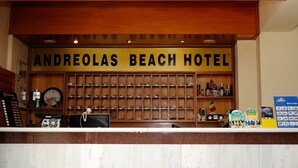 Receptionen på Andreolas Beach Hotel har en receptionsdisk i trä, en klocka och diverse bekvämligheter utställda på hyllor.