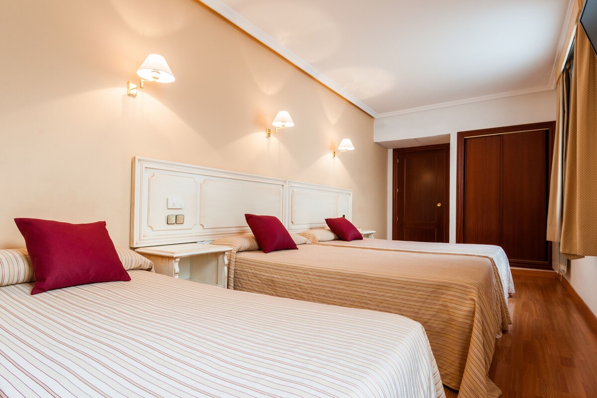 Habitación de hotel con dos camas, un armario de madera y luces fijadas a la pared.