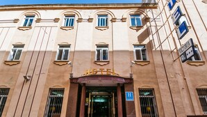 A hotel entrance with a classic facade, large windows, and a sign indicating a parking area. - Victoria (Linares)