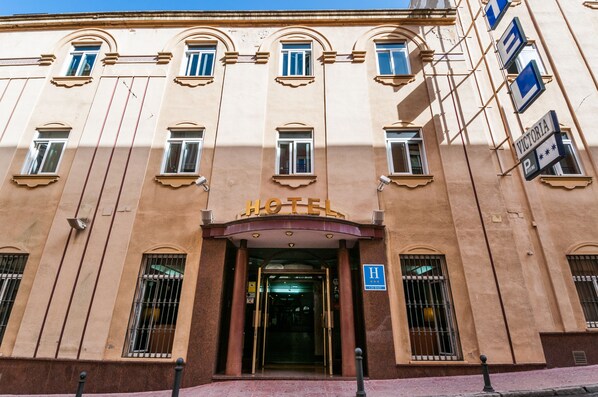 Entrada de hotel con fachada clásica, ventanas grandes y un letrero que indica una zona de estacionamiento.