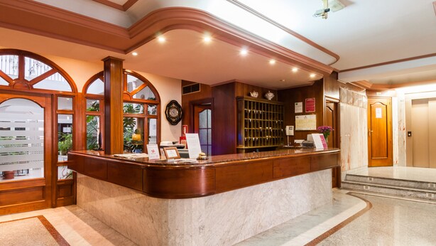 A reception area with a marble counter, wooden paneling, and a clock on the wall. - Victoria (Linares)