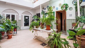 A spacious courtyard with a white tiled floor, multiple potted plants, and a central table. - Victoria (Linares)