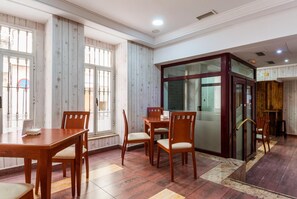 Habitación de hotel con piso de madera, comedor con mobiliario de madera, ventanas amplias y un ascensor de vidrio.