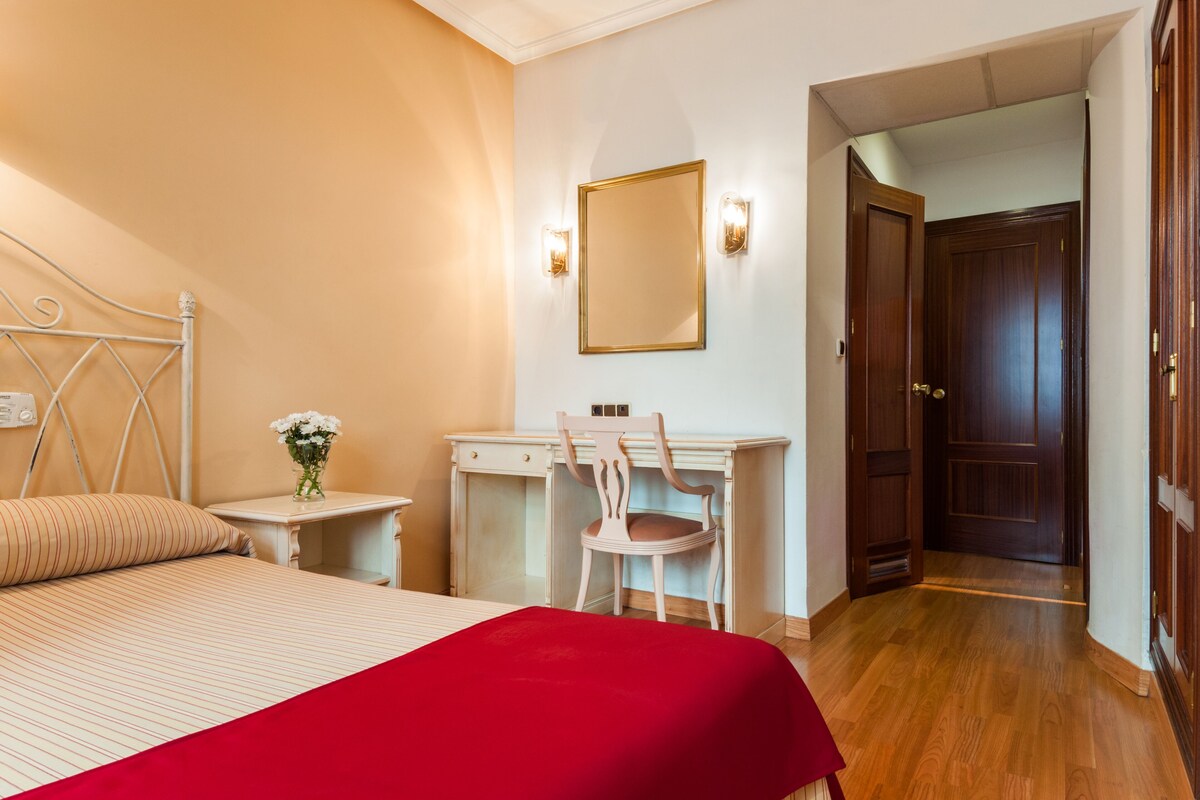 Habitación de hotel con una cama, un escritorio, una silla y una puerta que da a otra habitación.