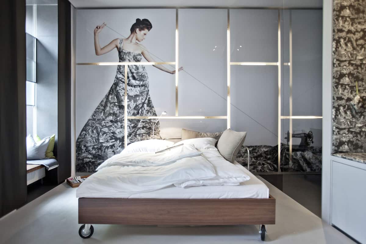 A modern bedroom with a large bed, a wall-mounted TV, and a decorative wall panel.