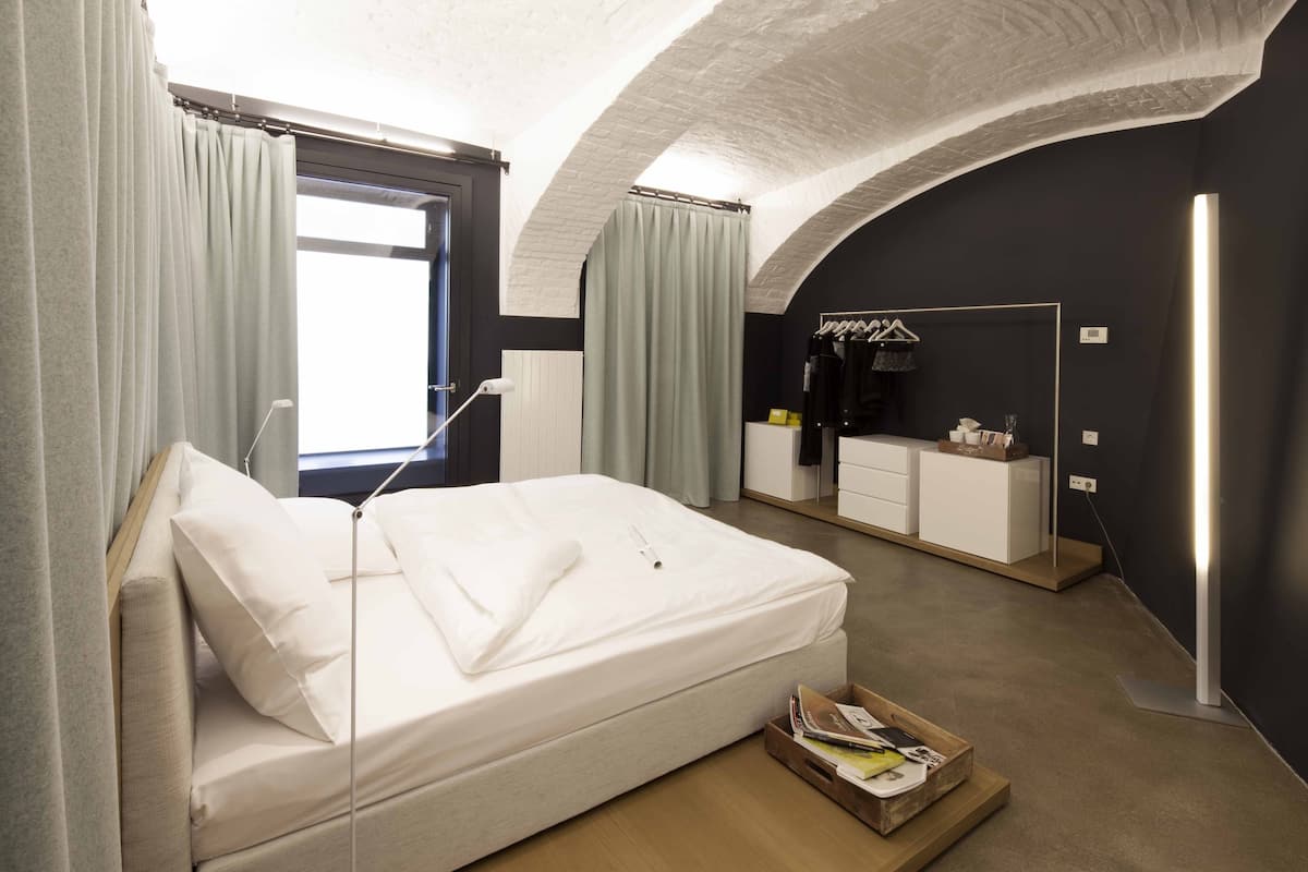 A modern hotel room with a bed, a vanity with a mirror, and a bedside table.