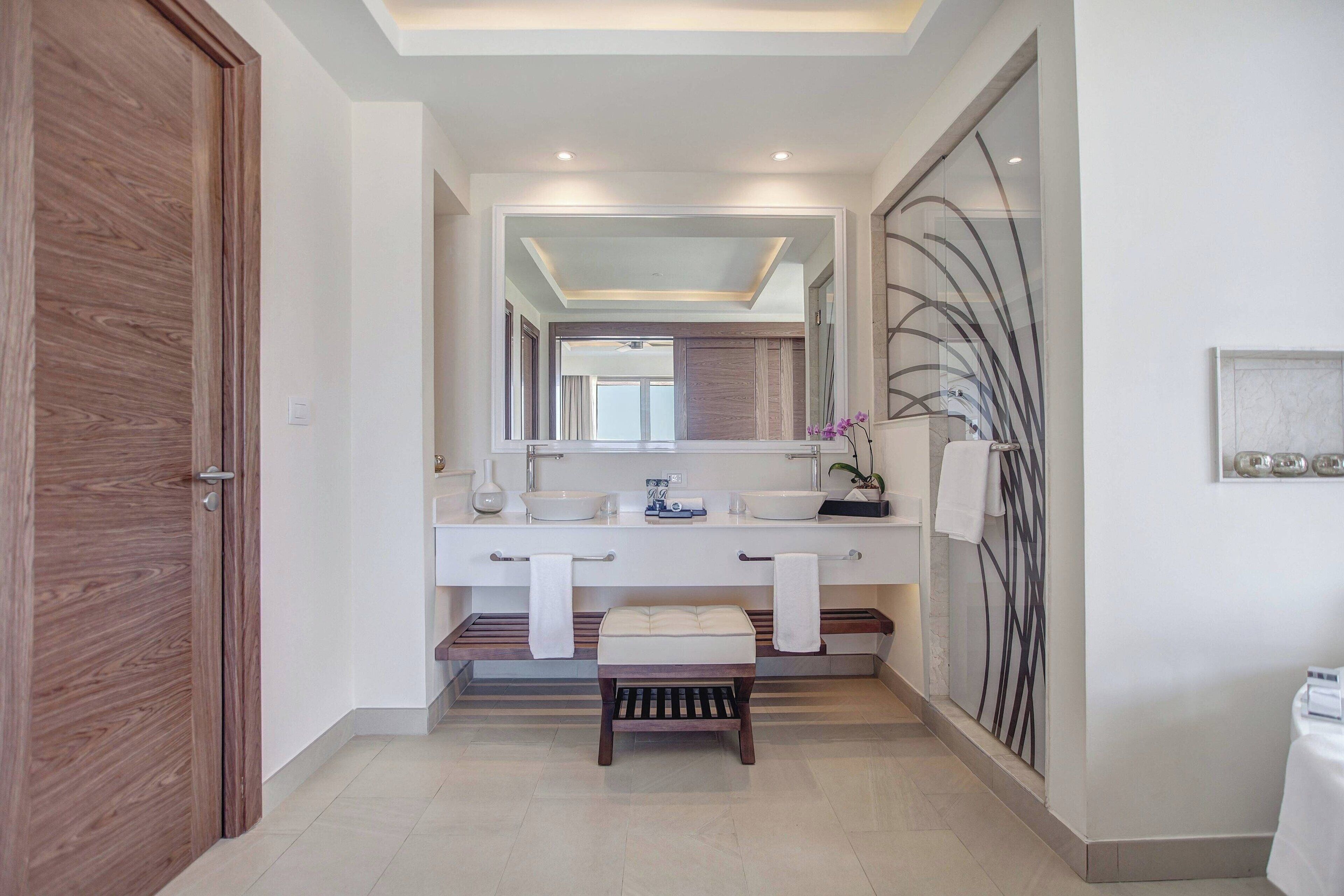Un baño moderno con tocador doble, una banca y un espejo grande.