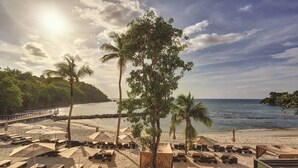 Un complexe hôtelier en bord de mer, doté de chaises longues, de parasols et d’un palmier.