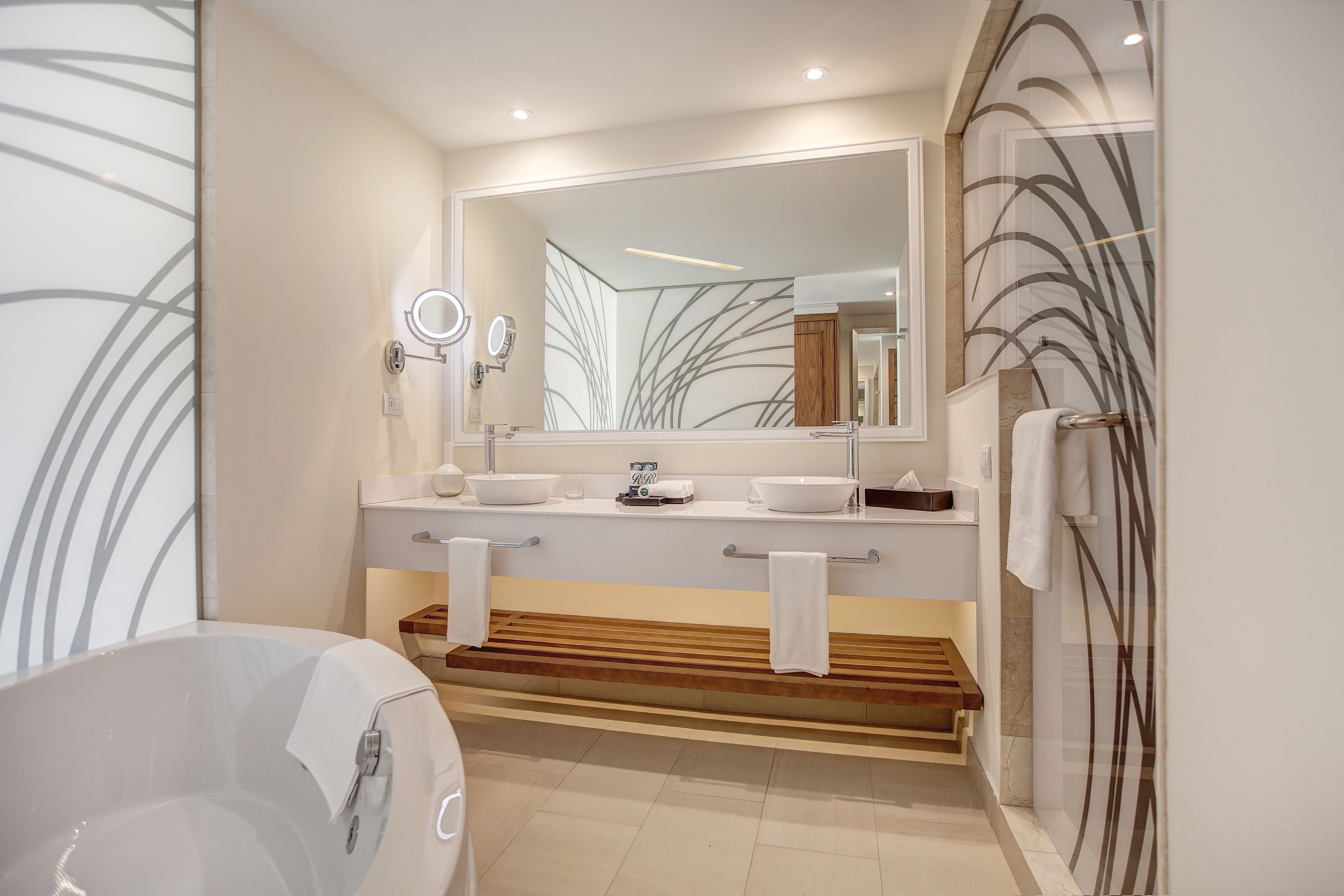 Une salle de bain moderne avec un grand miroir, deux lavabos, une baignoire et un espace douche.