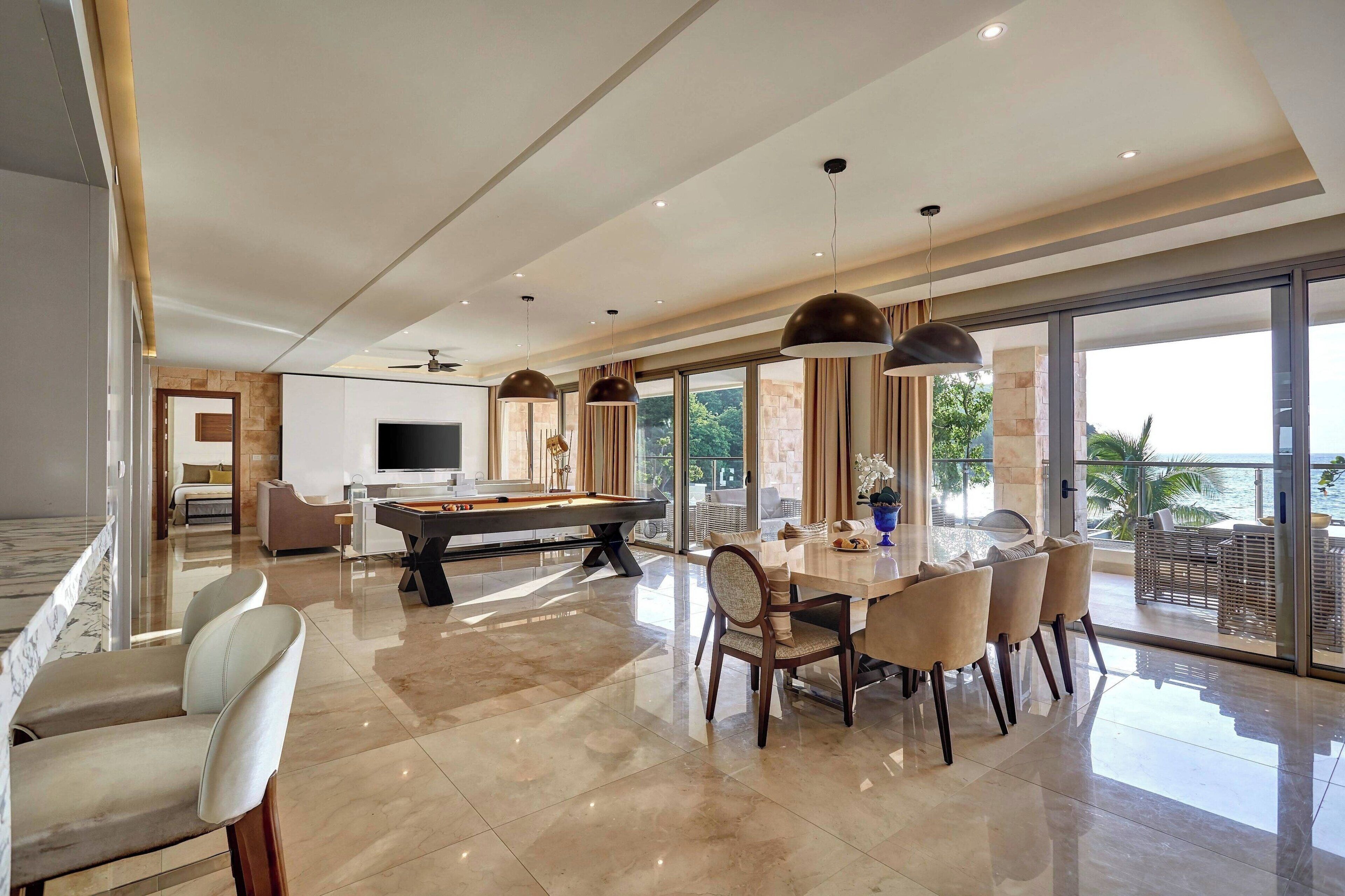 A spacious living area with a pool table, dining table, and chairs. There is a TV and a sofa in the background.