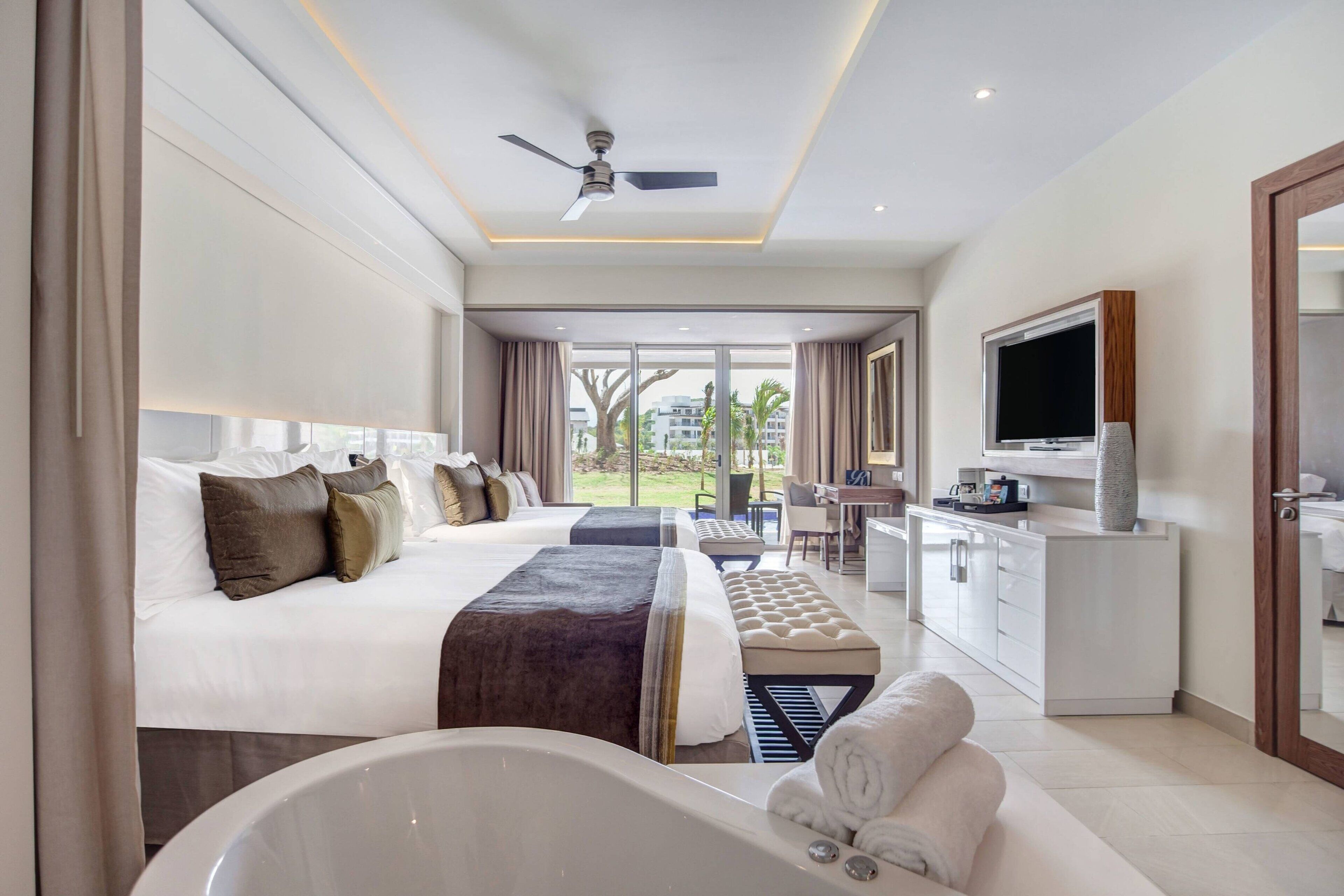 Una habitación de hotel moderna con una cama grande, un sofá independiente, un escritorio, un televisor y una bañera.