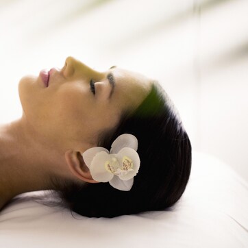 A person lying on a white pillow with a white flower accessory.