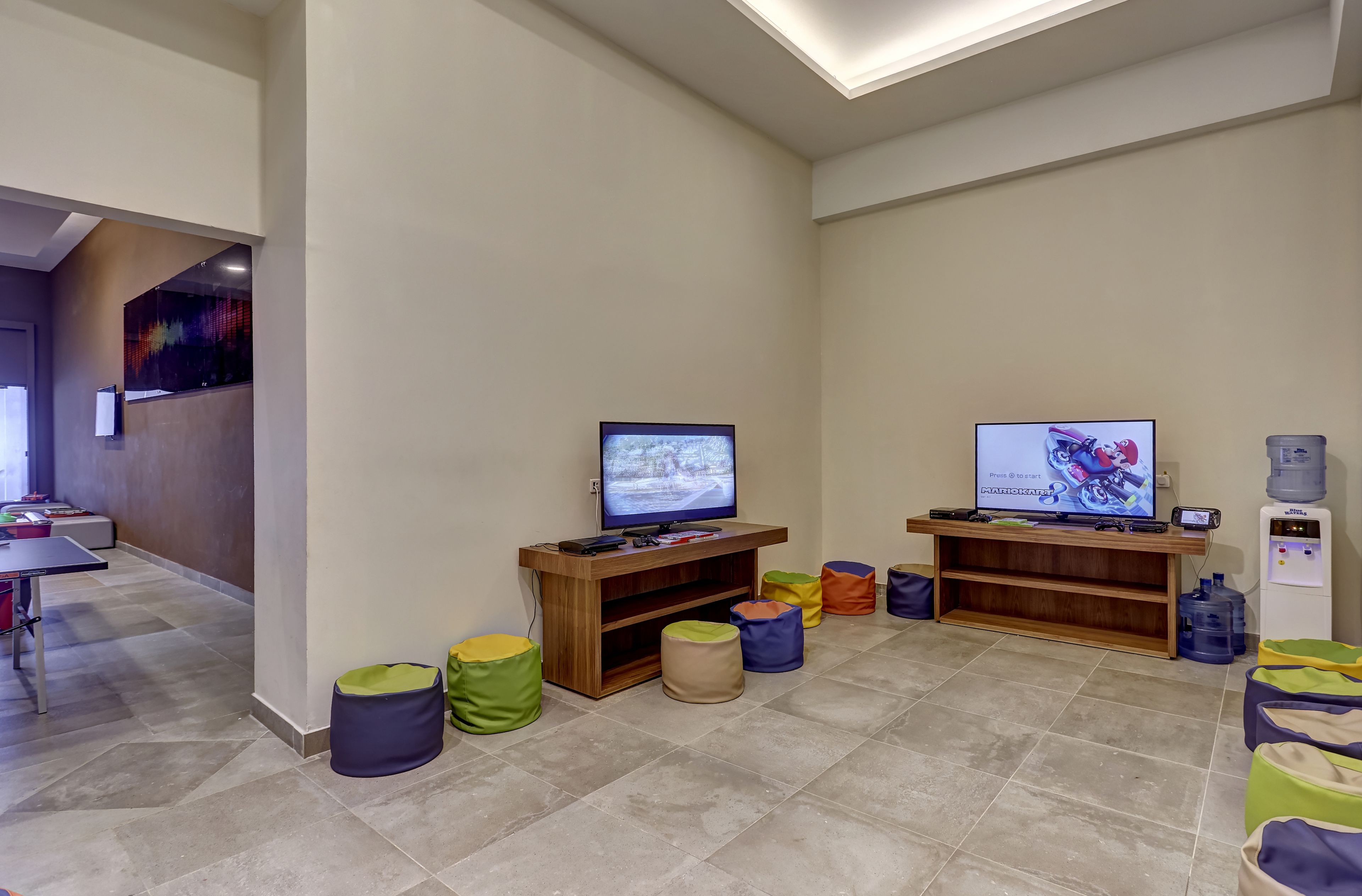 A modern living room with two televisions, a water dispenser, and colorful bean bags.
