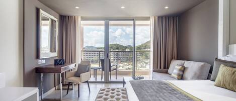 Habitación de hotel moderna con una cama grande, un escritorio y vistas a un paisaje urbano a través de amplias ventanas.