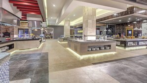 A modern hotel lobby with a central island counter, seating areas, and a visible kitchen area.