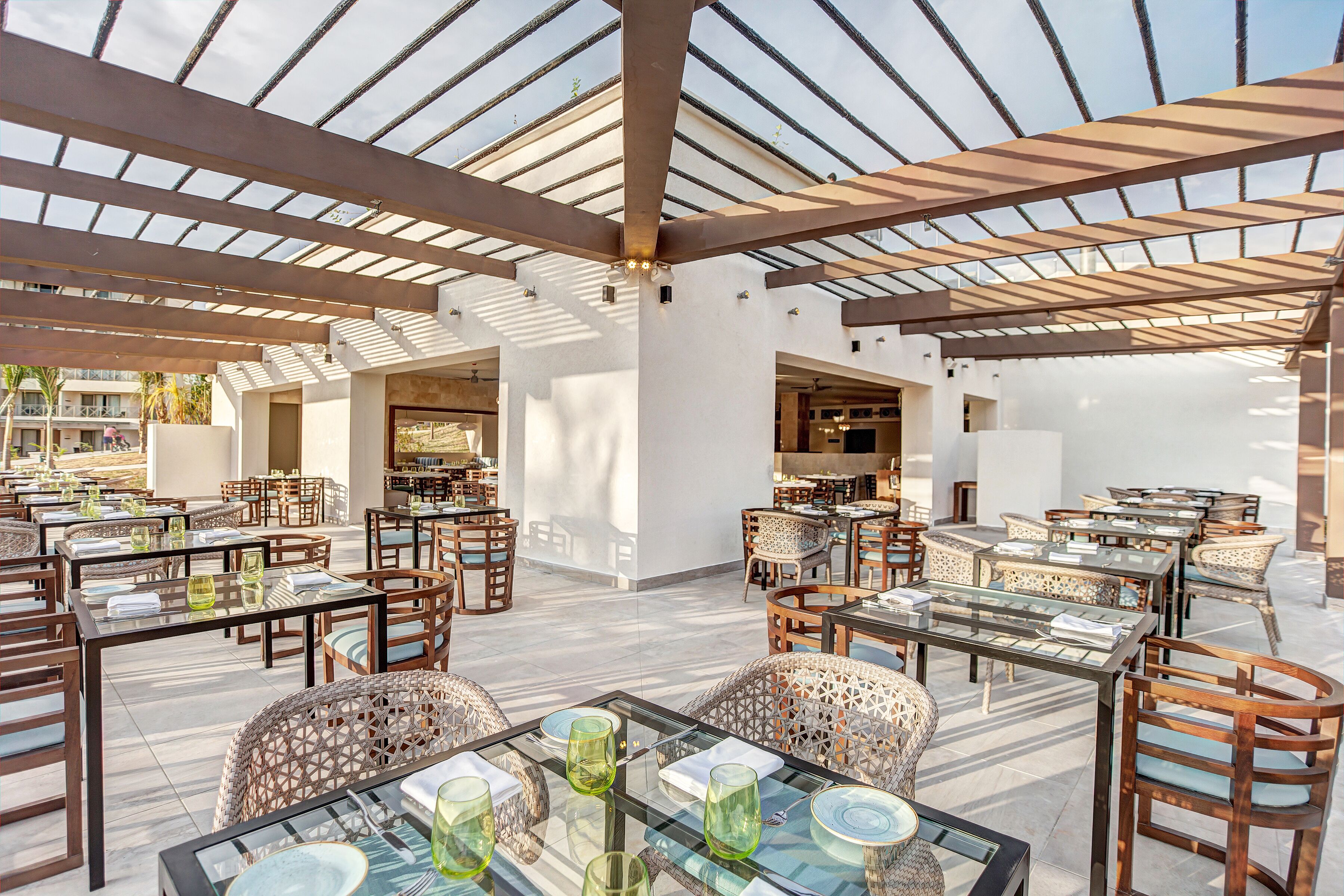 An outdoor dining area with multiple tables and chairs, a glass ceiling, and a view of the surrounding buildings.