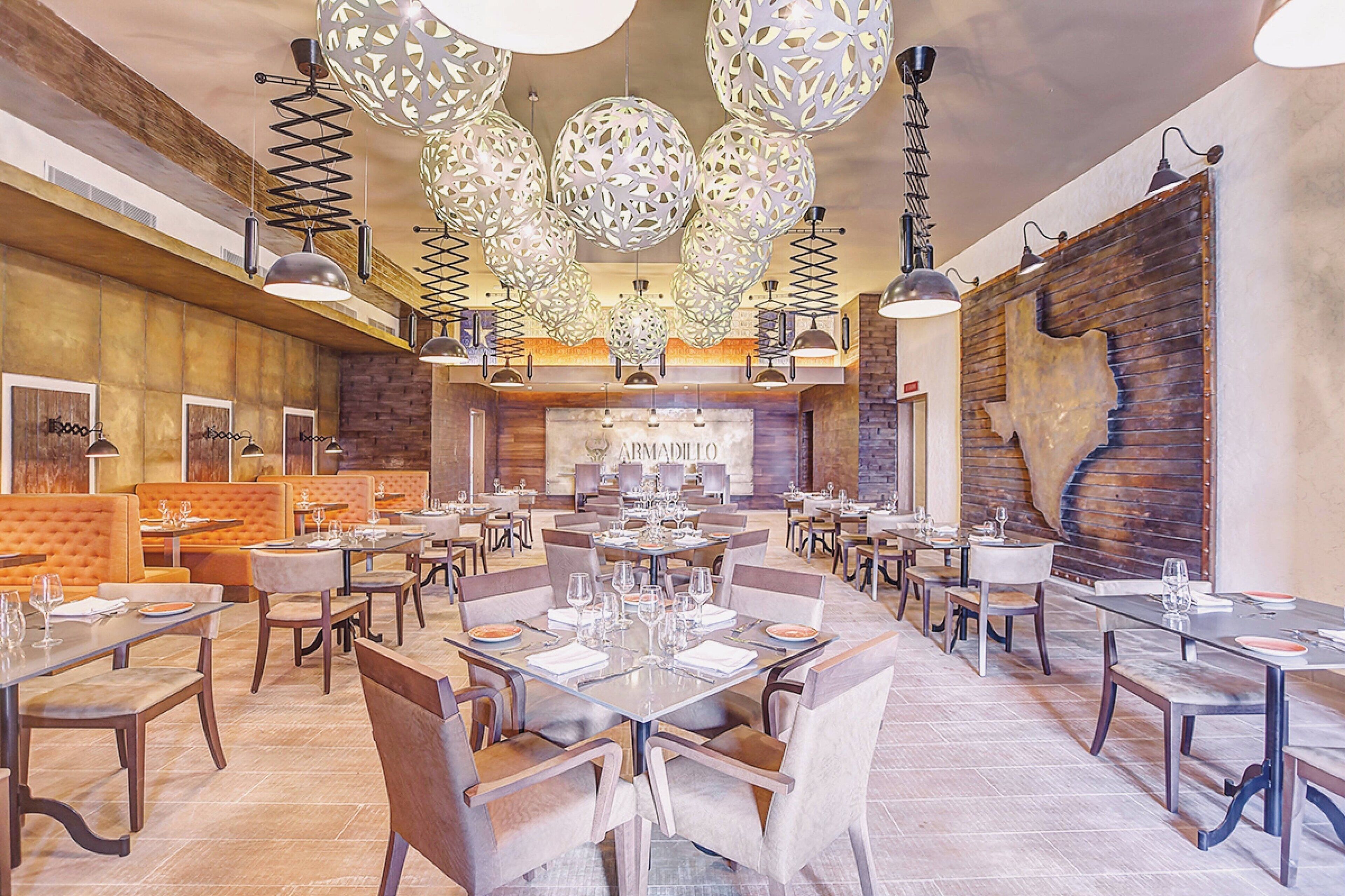 Un restaurante espacioso con varias mesas y cabinas, iluminación colgante moderna y una pared de madera rústica.