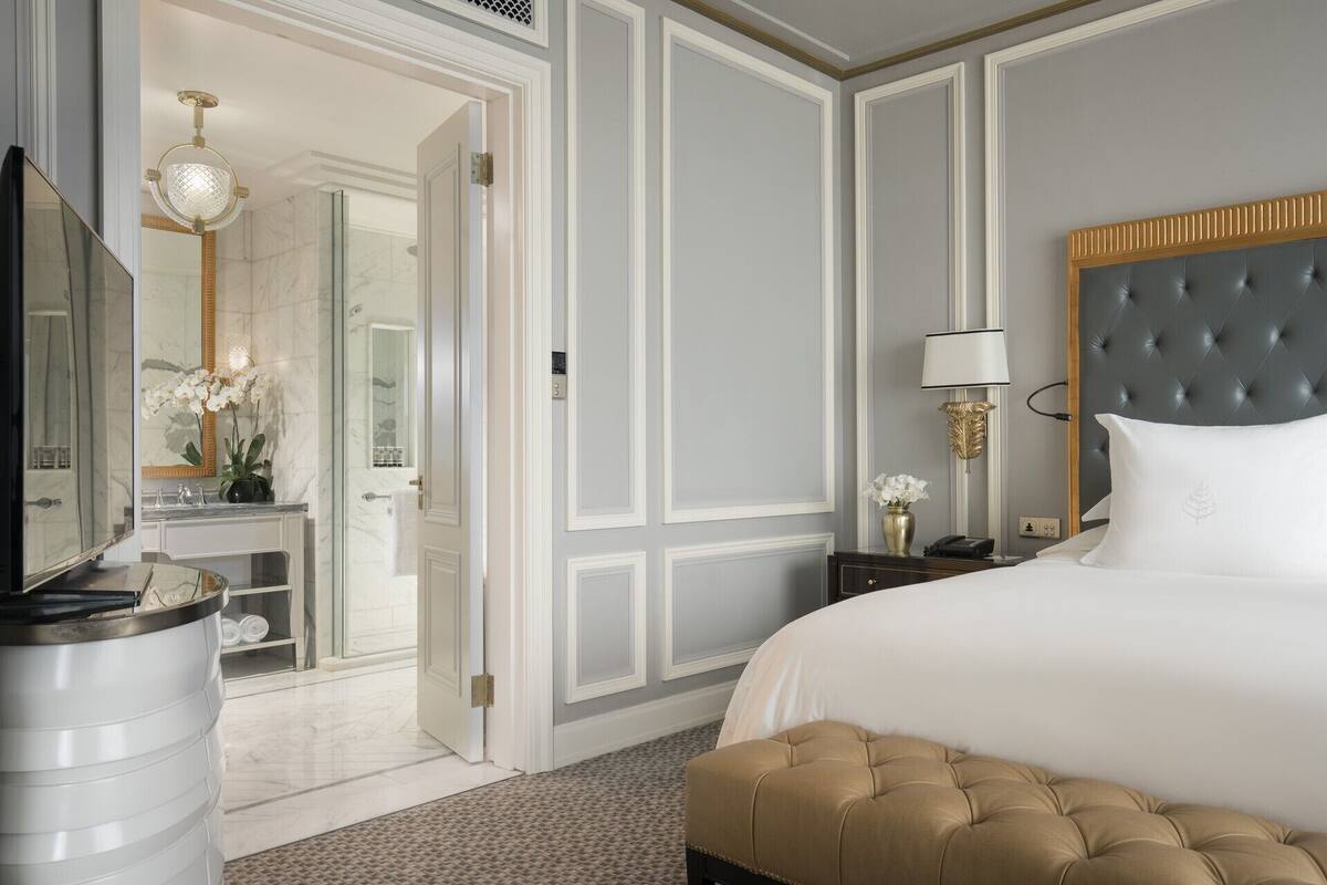 Hotelkamer met een groot bed, een nachtkastje met een lamp, een spiegel en een zichtbare badkamer door een geopende deur.