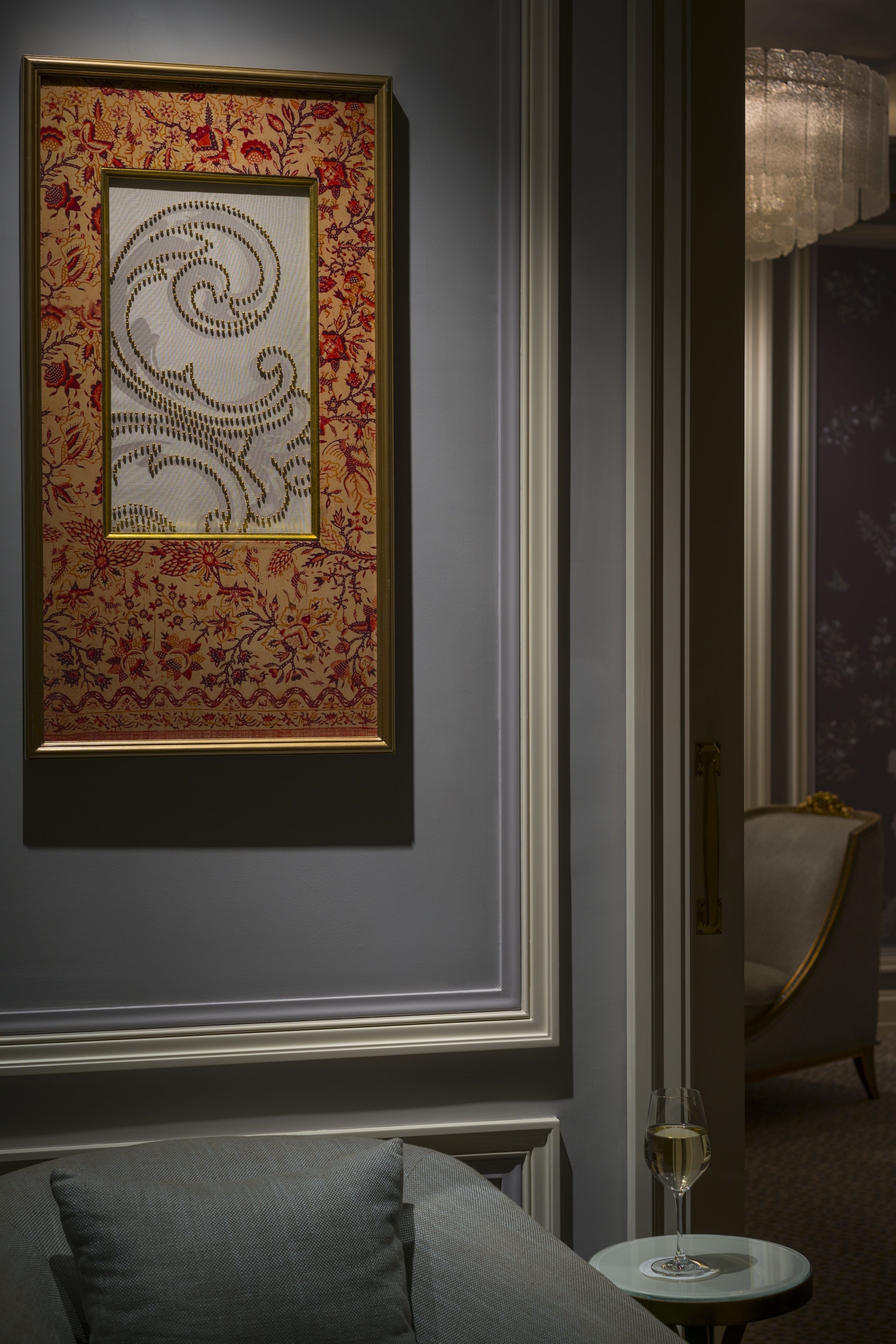 A framed artwork on a wall, a chair, and a small table with a glass of water.