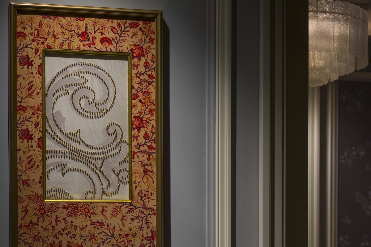 Une œuvre d’art encadrée accrochée au mur, une chaise et une petite table avec un verre d’eau.