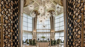 Een luxe lobby met een ronde centrale tafel, stijlvolle groene stoelen en een decoratieve metalen scheiding.