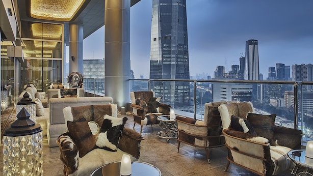 Een hotel lobby met hoge plafonds, lederen banken, een glazen balustrade en uitzicht op de skyline van de stad.