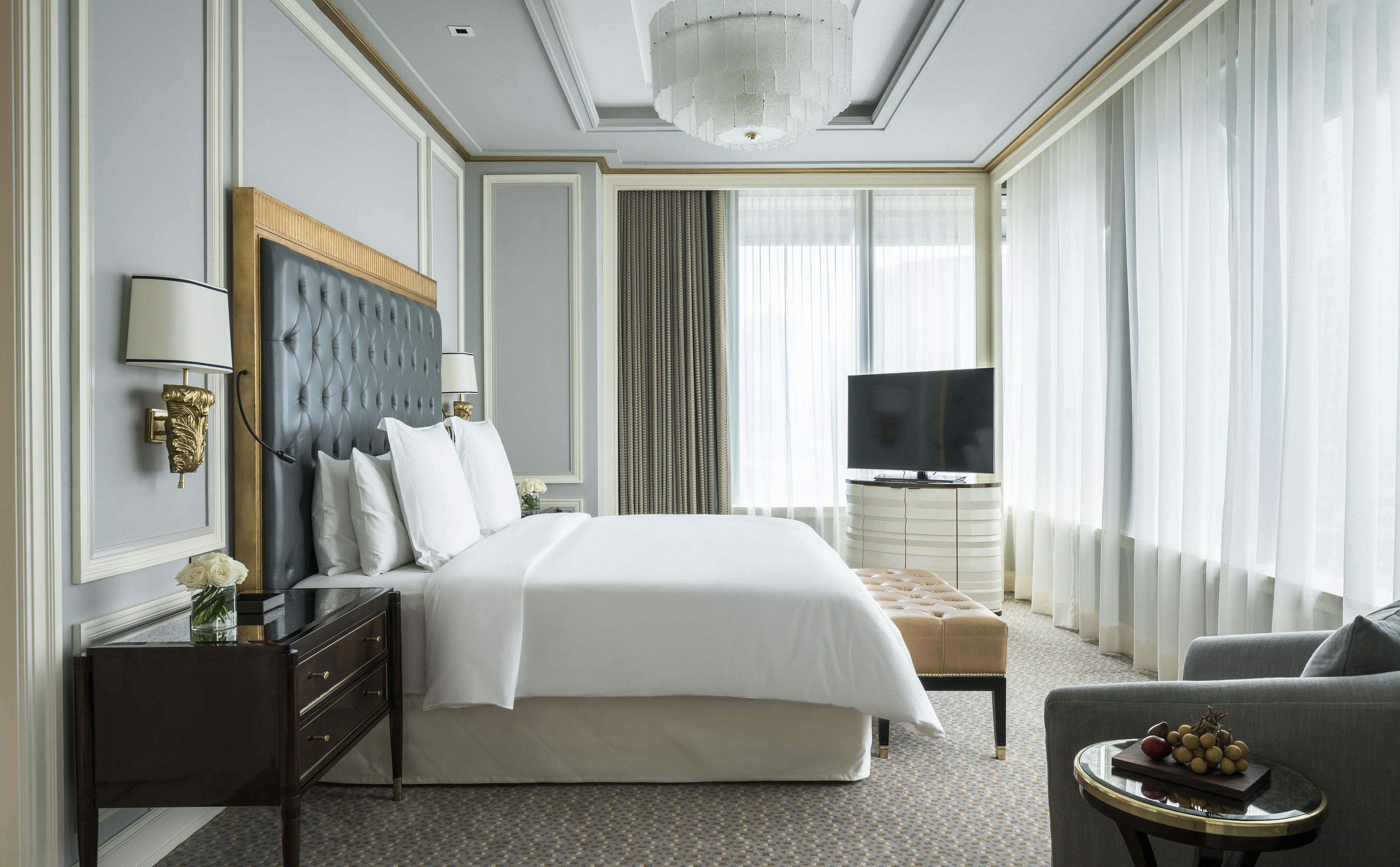 A hotel room with a large bed, a TV, a seating area, and a chandelier.