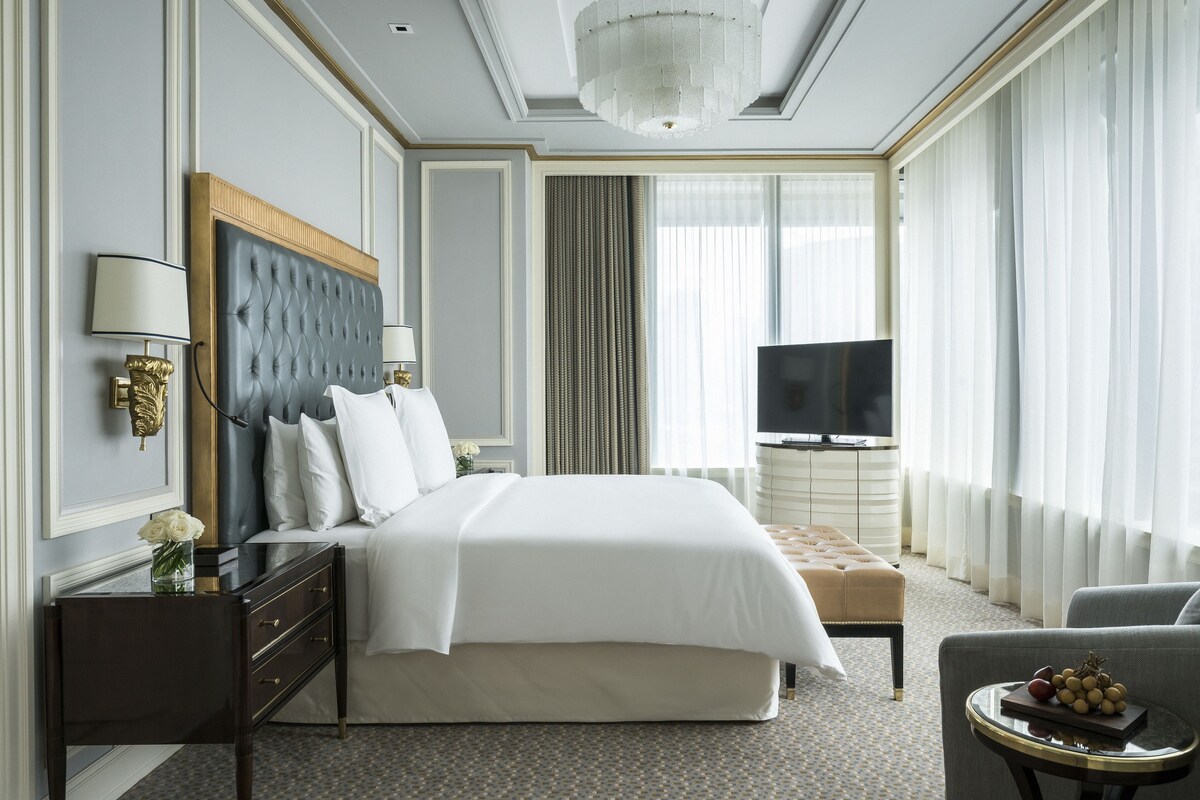 Une chambre d’hôtel dotée d’un grand lit, d’une télévision, d’un coin salon et d’un lustre.