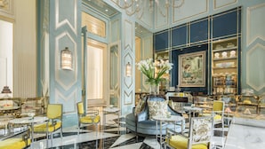 Een luxueuze lobby met een blauw en goud kleurenschema, met een kroonluchter, zithoeken en een presentatie van decoratieve objecten.