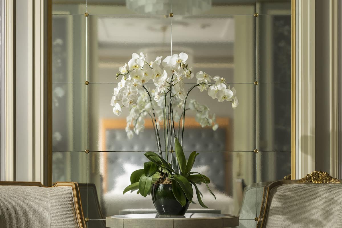 Een kamer met een ronde tafel, twee fauteuils en een vaas witte orchideeën.