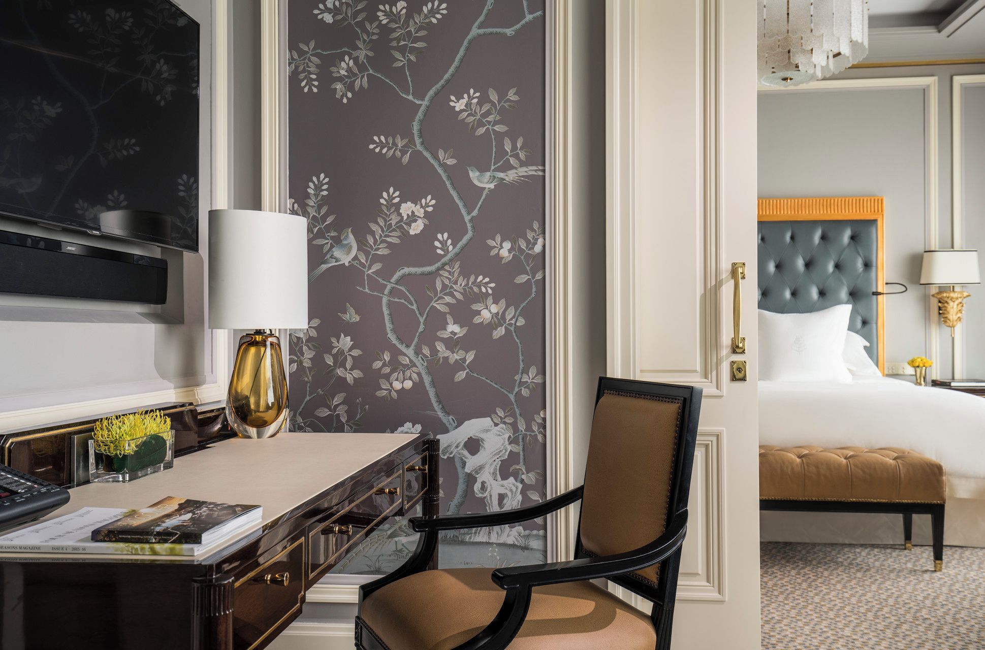 A hotel room with a desk, chair, bed, and a large window.