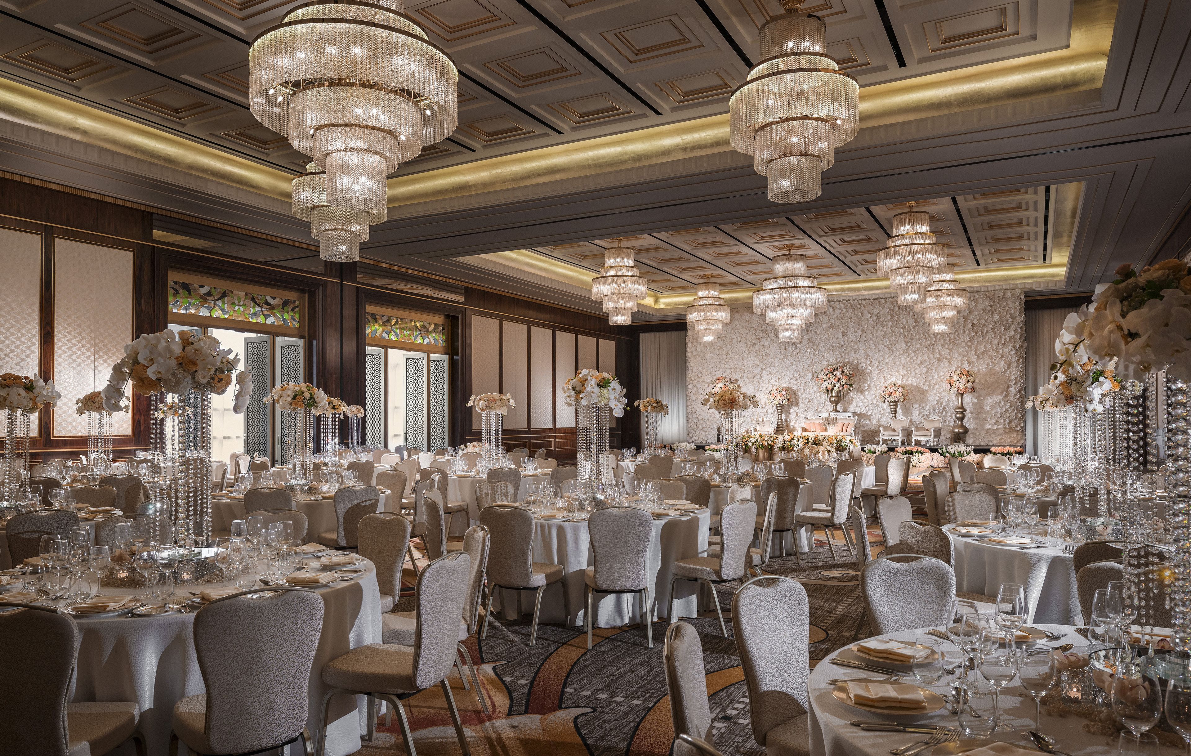 A banquet hall with round tables set for dining, chandeliers, and floral centerpieces.