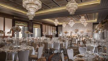A banquet hall with round tables set for dining, chandeliers, and floral centerpieces.