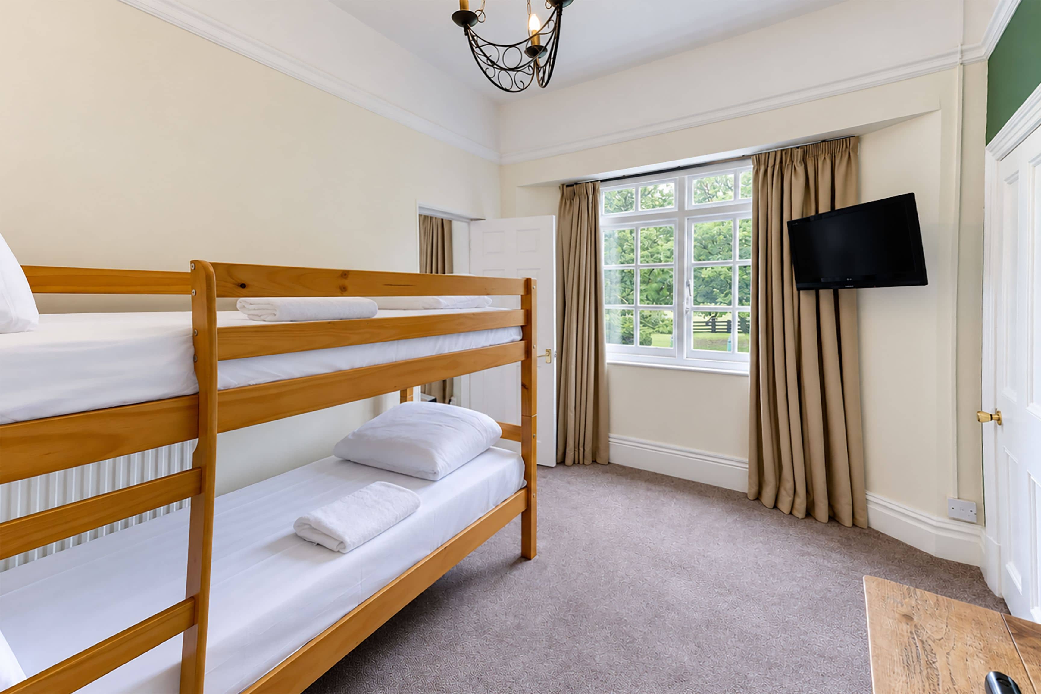 A room with bunk beds, a television, and a window with curtains.