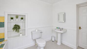 Une salle de bain avec des toilettes, un lavabo et des étagères ornées de plantes.