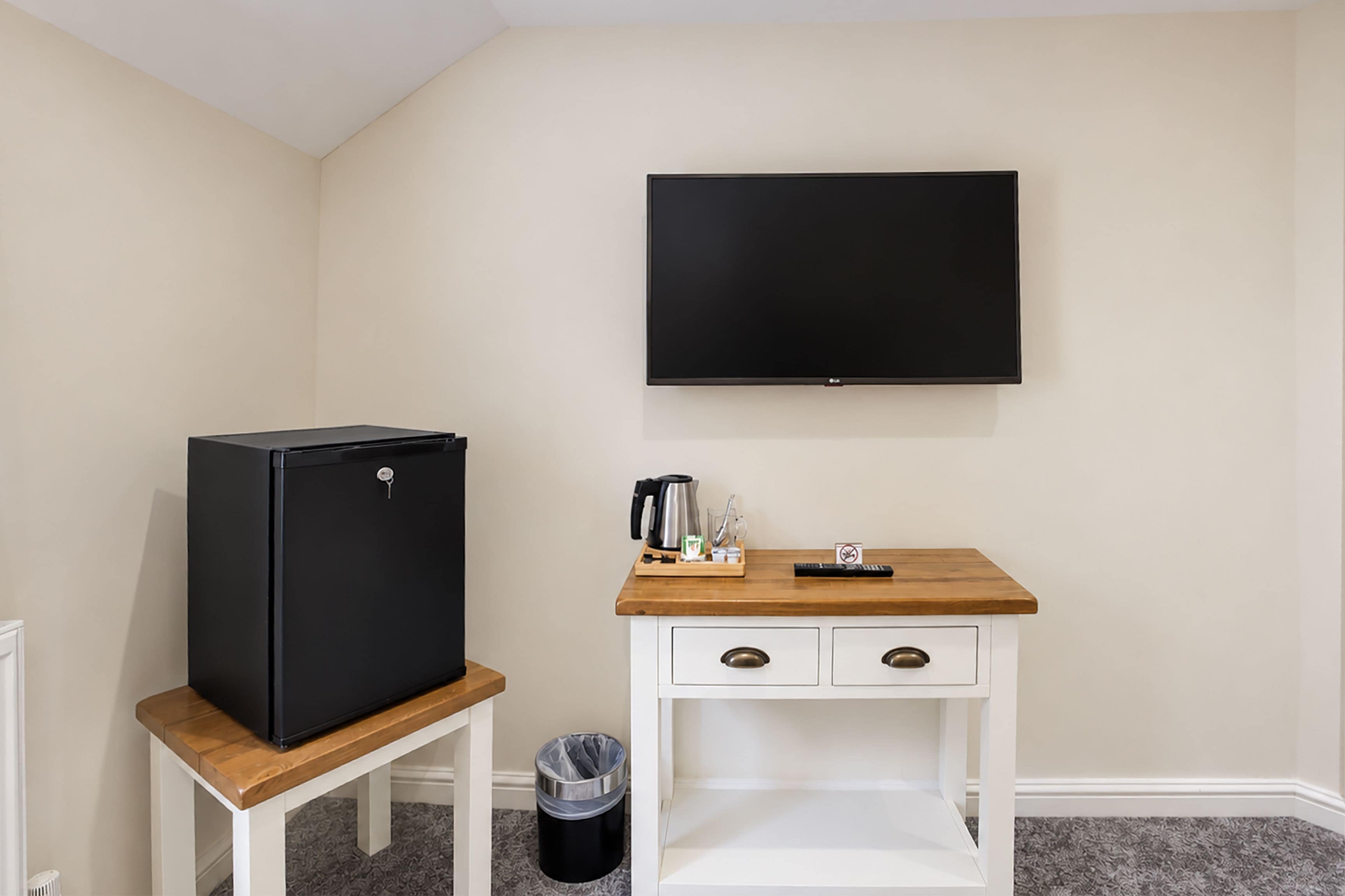 Una kitchenette compacta con un refrigerador negro, una cafetera y una pequeña mesa de madera.