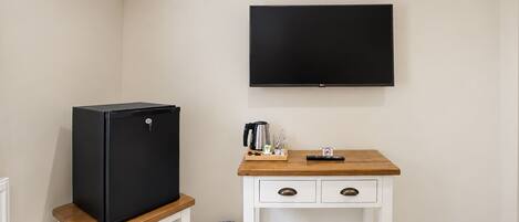 Una kitchenette compacta con un refrigerador negro, una cafetera y una pequeña mesa de madera.