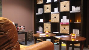 Een gezellige zithoek met lederen fauteuils en tafels, een boekenkast met diverse spullen, en kaarsen op de tafels.