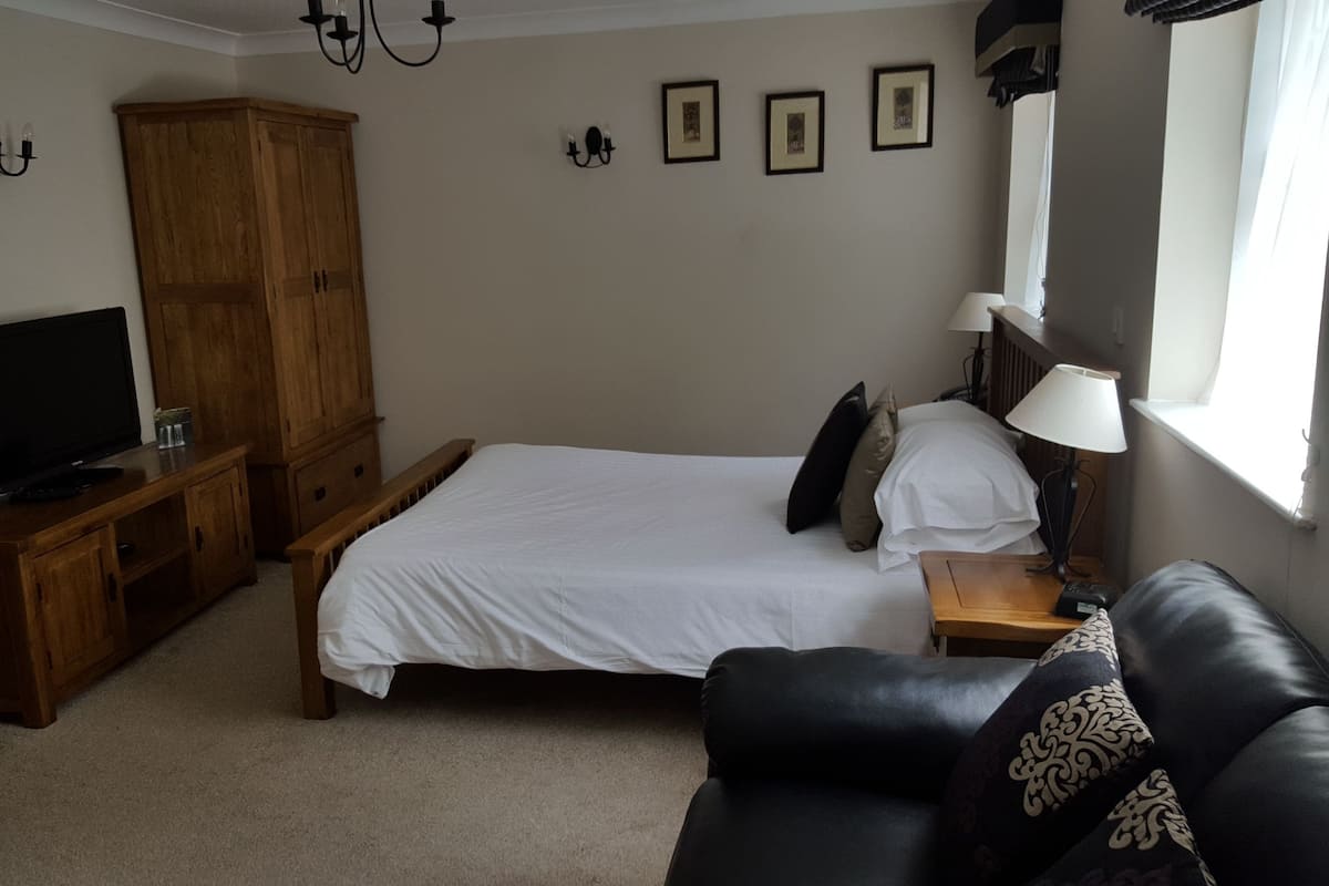 Ein Schlafzimmer mit einem Bett, einem Holzschrank, einem Fernseher, einem Schreibtisch und einem Fenster.