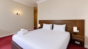 A neatly made bed with white linens, two bedside lamps, and a folded towel on the footboard.