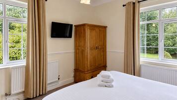 A bedroom with a bed, a wooden wardrobe, a television on the wall, and windows with curtains.